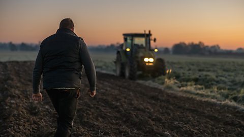 A farmer walking through a field to a tractor at sunset