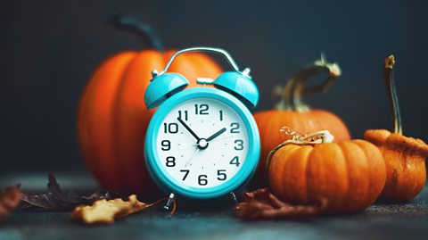 A teal coloured alarm clock surrounded by pumpkins