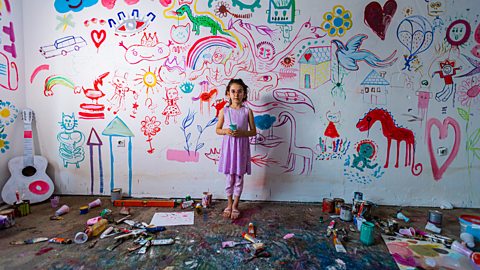 Child in front of a wall covered in paintings.