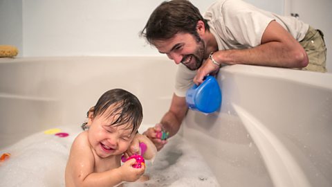 A dad and their baby play during bathtime using bath toys