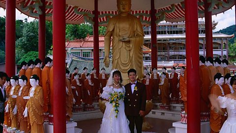 A newly married couple in Malaysia visiting a Buddhist temple. The couple are wearing wedding clothes. 