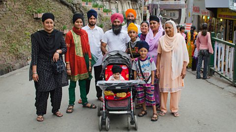 An extended Sikh family stood together in a shopping street. Includes grandparents, parents and children and babies.