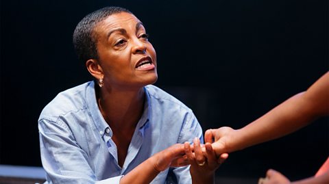 A middle-aged black woman with short hair wearing a blue shirt. She is reading someone's palm.