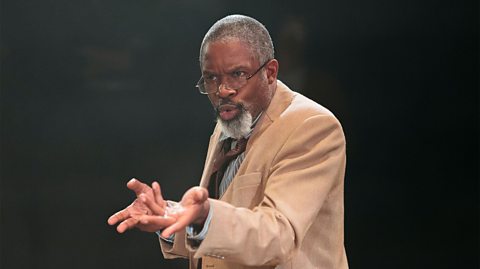 A middle-aged black man with short, greying hair and a goatee beard. He is wearing glasses and a cream coloured jacket, with a shirt and tie.