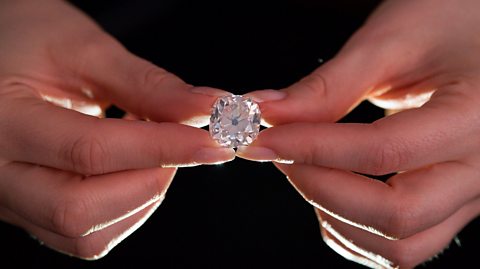 A pair of hands holds the 26-carat diamond, with the jewel positioned centrally in the image.