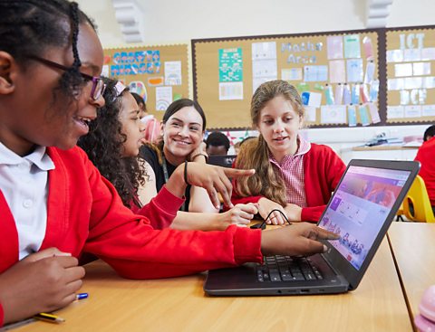 Three primary school children look at a coding platform on a laptop as their teacher looks on