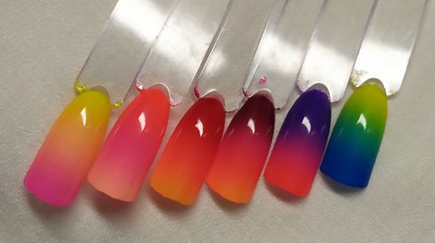 A series of colorful artificial nails in ombre colours next to one another.