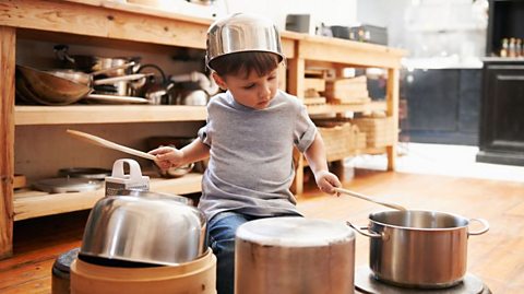 A little boy playing drums on metal pots and pans.