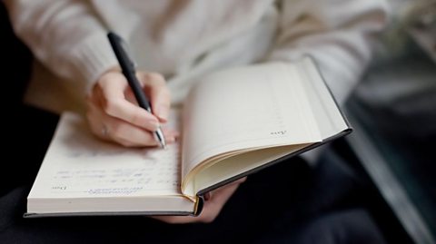 Close-up of a woman writing in a notebook with a black pen.