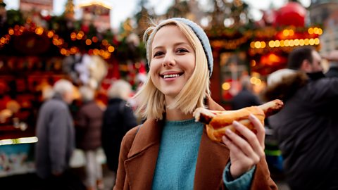 Woman at a christmas market holding a sausage in a roll
