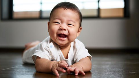 A Japanese baby lying on their front, smiling at the camera.