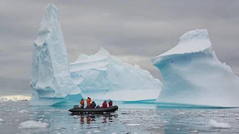 Mint Images-David Schultz/Getty Images People in a zodiac in front of two icebergs on the Antarctic Peninsula
