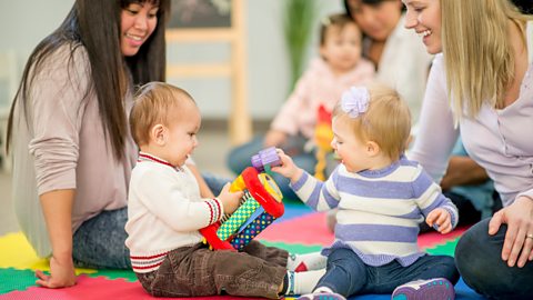 Two mums supervise their babies playing with toys at a library club .