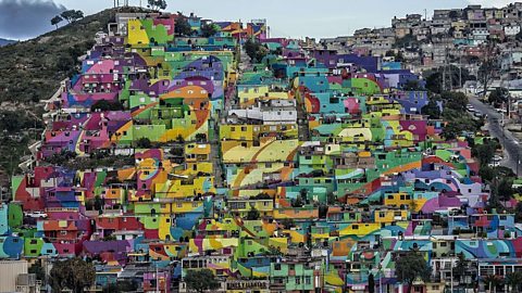 A hill covered in colourful small houses, all very near each other. They have been painted in yellow, purple, blue and other bright hues.