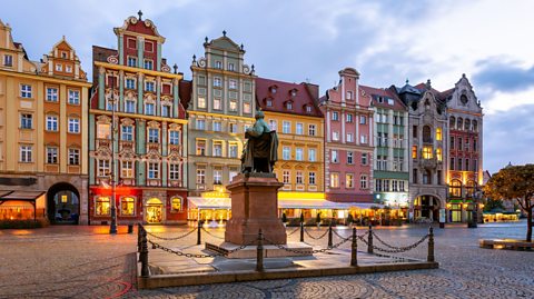 Tall buildings painted in different pastel hues face a statue on a cobbled street in Wroclaw, Poland