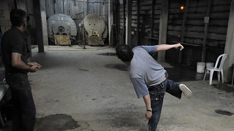 A tejo player stands on one leg after throwing the tejo puck towards the cancha target.