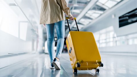 A person at an airport wheeling a yellow suitcase behind them.