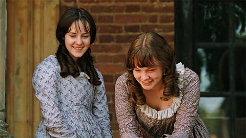 Two young girls with curled hair stand together, smiling