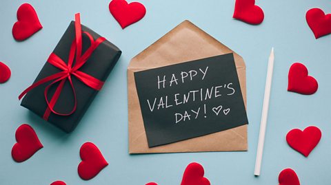 A valentines day card and present on a pastel blue backdrop, surrounded by love hearts.