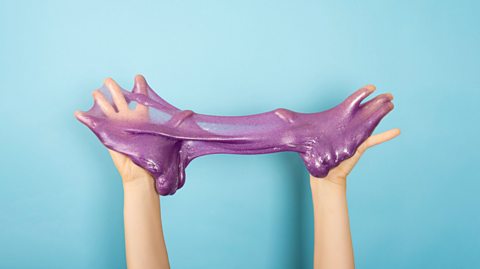 Close up of shiny purple slime in the hands, on blue background. 