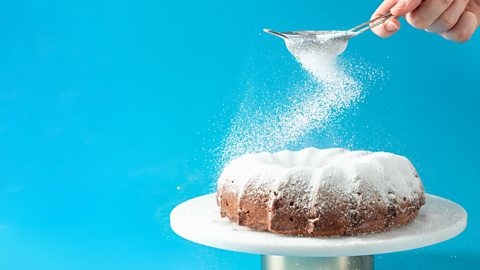 A woman's hand dusting a round cake on blue background.