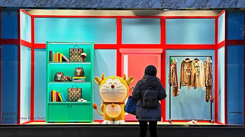 Getty Images Um pedestre passa por uma figura de Doraemon exposta na vitrine de um Spa Gucci.