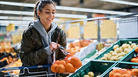 A woman in a supermarket adds a bag of oranges to her trolley 