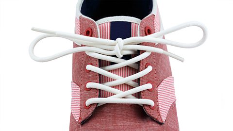 Close up of a red canvas shoe with white laces tied in a bow