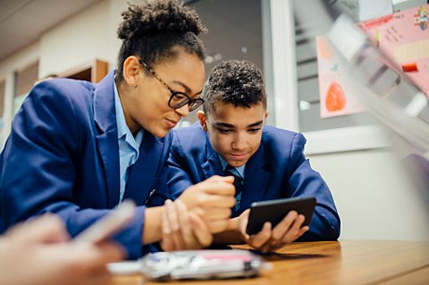 Two students looking at a mobile phone screen in a classroom.