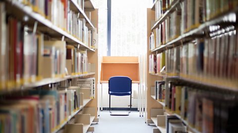 A blue chair in front of an orange desk in a university library surrounded by books.