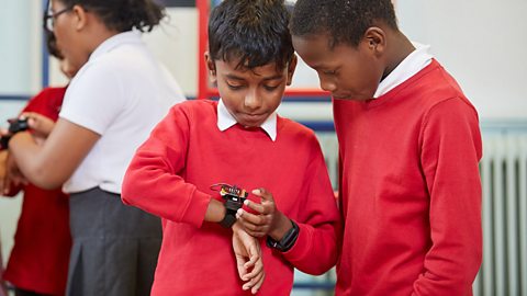 Two primary school children looking at a ý micro:bit attached to one of their wrists.