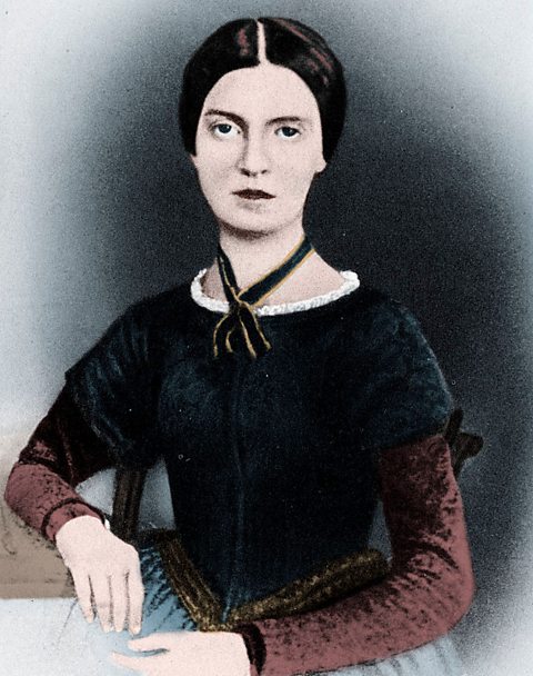 A portrait of a woman wearing a black top with burgundy sleeves. Her dark hair is tied back.