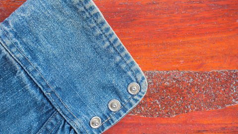 A close up of a denim shirt cuff with three press studs and lying on a wooden table