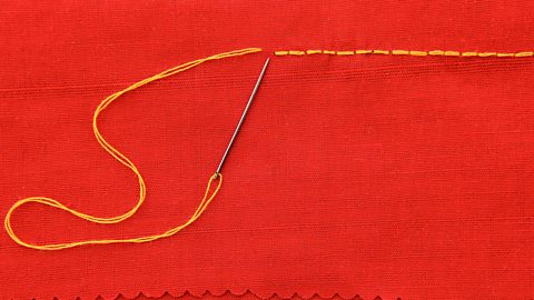 A piece of red fabric with a line of yellow backstitches running along the top, with a needle attached to the thread