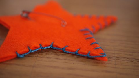 An orange felt star lying on a table, with a safety pin attached and a blue line of blanket stitches running along its edge