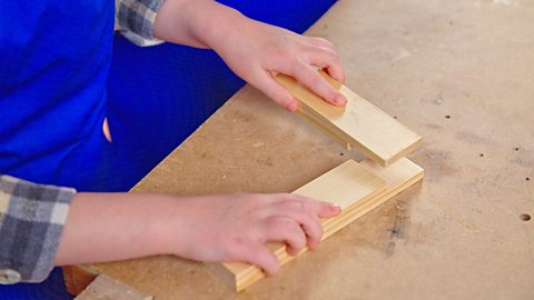 Hands positioning two pieces of cut wood to make a lap joint