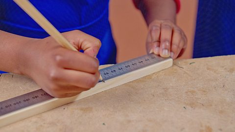 A child measuring and marking wood with a pencil and a metal ruler