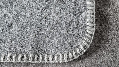 A grey fleece blanket with a blanket stitch around the edge