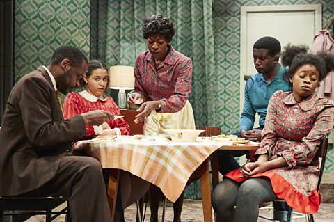 A family consisting of a man, woman and three children are sitting around a table eating dinner.
