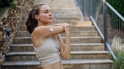 Woman standing on steps outdoors doing exercise while wearing a CGM