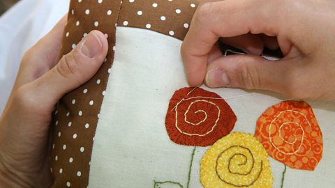 Close up of hands sewing an appliqué flower onto a cushion