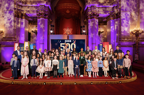 Her Majesty The Queen, the 50 finalists along with 500 Words official judges and hosts pose for a picture on the stage.