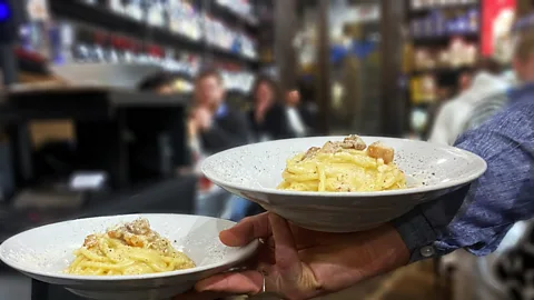 Andrea Carlo Martinez A waiter holds two plates of carbonara in Roscioli’s Salumeria restaurant (Credit: Andrea Carlo Martinez)