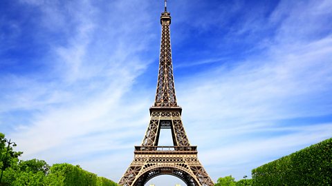 The Eiffel tower on a sunny day. A crowd on the grass at its base.