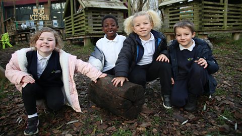 4 children in school uniform sat around a log outdoors