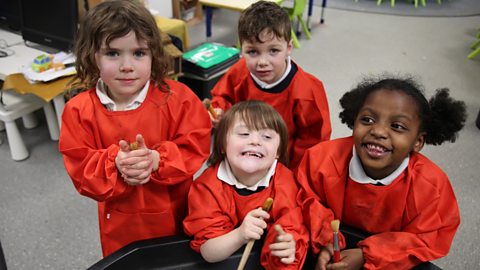 Four children in school uniform and red aprons holding paint brushes