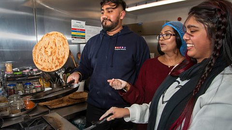 A South Asian man and two South Asian women cook food in a pan