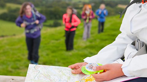 A group of teenagers on outdoor expedition holding map and compass