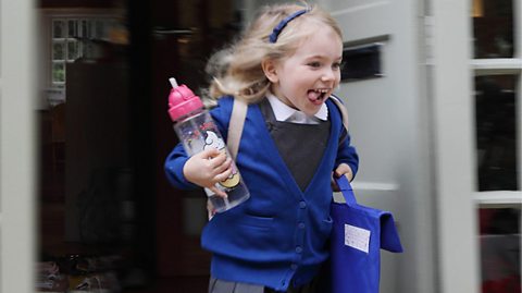 A young girl in school uniform runs out the door holding a bookbag