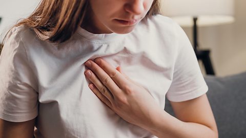 Woman sits with her hand on her chest, uncomfortable with heartburn